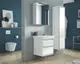 Weißes Waschbecken mit Unterschrank und Spiegelschrank in einem modernen Badezimmer mit blauer Wand, ausgestattet mit Ideal Standard Armaturen. Holzregal im Hintergrund.